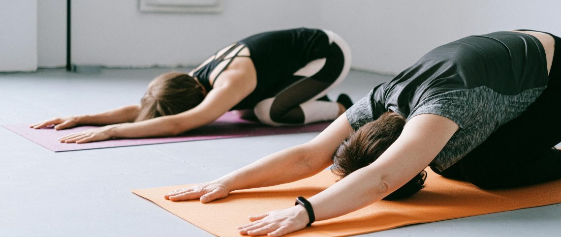 Two women practicing yoga indoors on colorful mats in a studio setting.